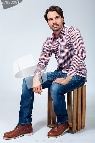 Image of Handsome young man sitting on a wooden box