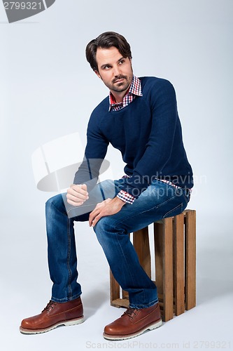 Image of Handsome young man sitting on a wooden box