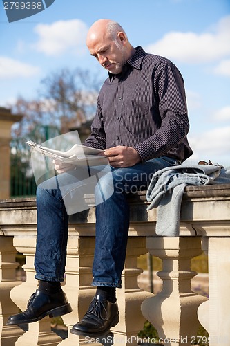 Image of Man sitting reading a newspaper on a stone wall