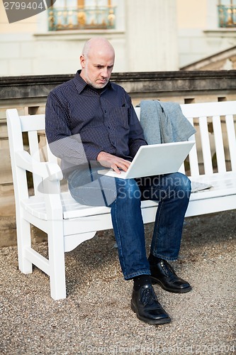 Image of Man sitting on a bench using a laptop