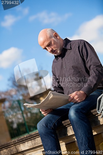 Image of Man sitting reading a newspaper on a stone wall