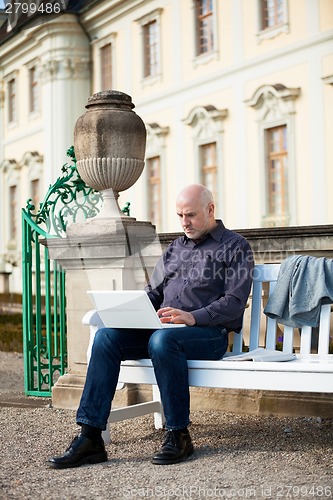 Image of Man sitting on a bench using a laptop