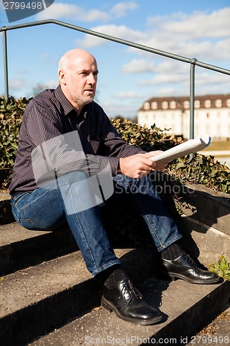 Image of Man sitting on steps reading a newspaper