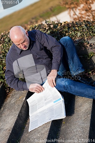 Image of Man sitting on steps reading a newspaper