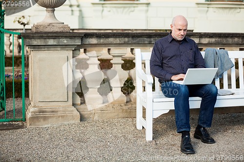 Image of Man sitting on a bench using a laptop