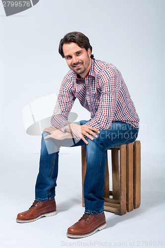 Image of Handsome young man sitting on a wooden box