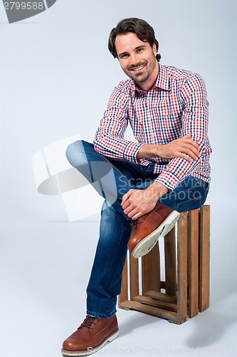 Image of Handsome young man sitting on a wooden box