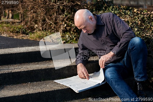 Image of Man sitting on steps reading a newspaper