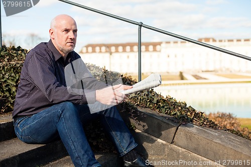 Image of Man sitting on steps reading a newspaper