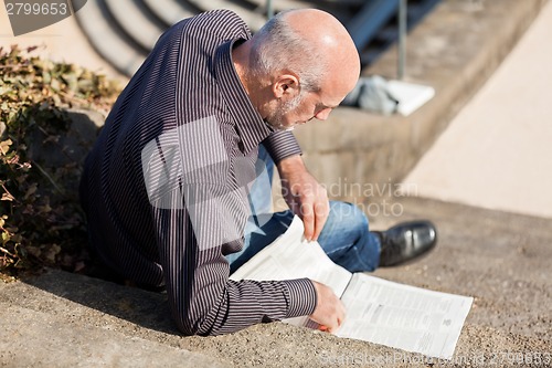 Image of Man sitting on steps reading a newspaper