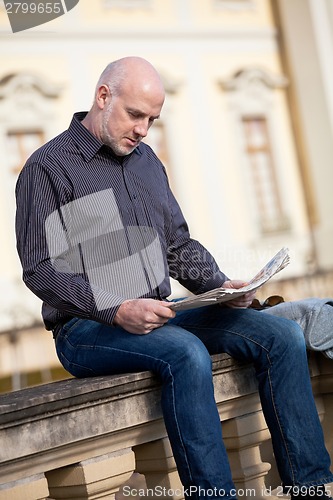 Image of Man sitting reading a newspaper on a stone wall