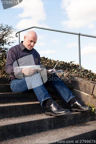 Image of Man sitting on steps reading a newspaper