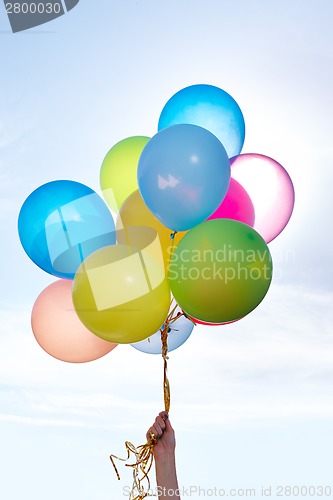 Image of Hand holding bunch of colorful balloons in blue sky