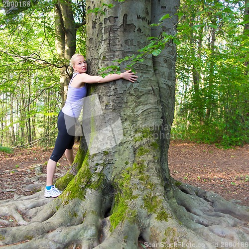 Image of Young woman hugging a tree.