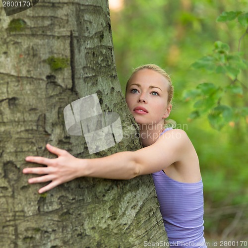 Image of Young woman hugging a tree.