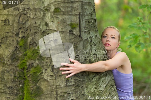 Image of Young woman hugging a tree.