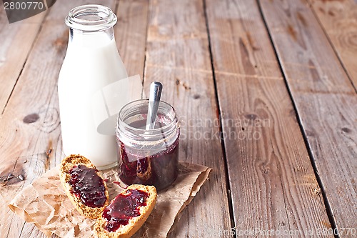 Image of black currant jam in glass jar, milk and crackers