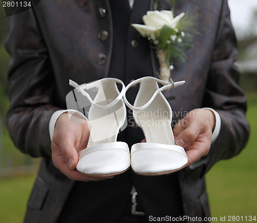 Image of Groom is holding bridal shoes