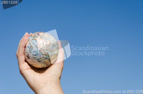 Image of global earth toy in hand on blue sky background  