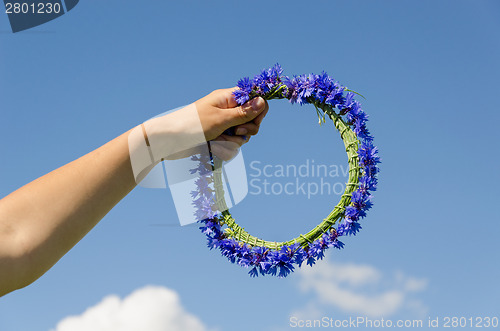 Image of hand hold cornflower crown in blue sky background