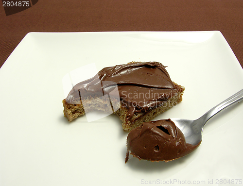 Image of Bitten into a wholemeal bread with hazelnut spread on a plate with little spoon