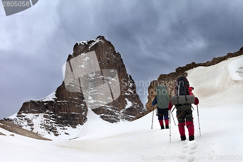 Image of Two hikers in snowy mountains and storm sky