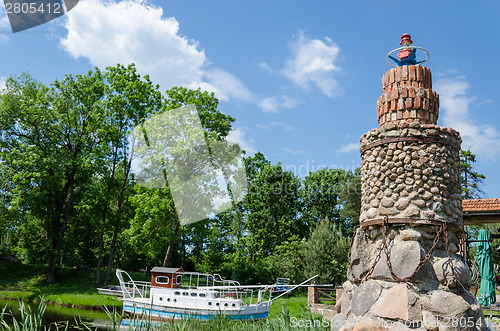 Image of stone brick lighthouse in summer park on blue sky 