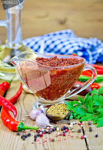 Image of Adjika in glass gravy boat on board with oil