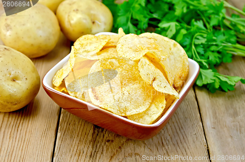 Image of Chips in clay bowl with potatoes on board