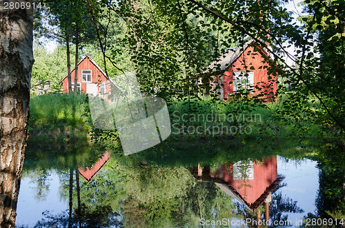 Image of red rural home reflected through branches on pond 