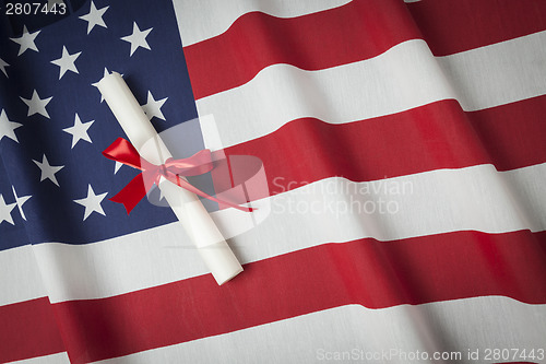 Image of Ribbon Wrapped Diploma Resting on American Flag with Copy Space
