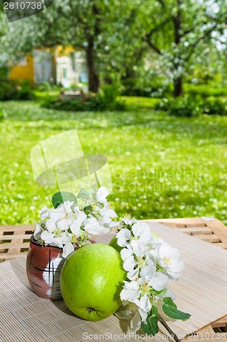 Image of Green apple with a branch of a blossoming apple-tree. On a table