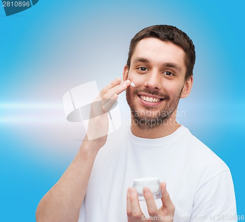 Image of beautiful smiling man applyin cream