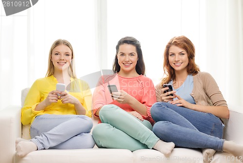 Image of smiling teenage girls with smartphones at home