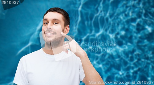 Image of smiling young handsome man pointing to cheek