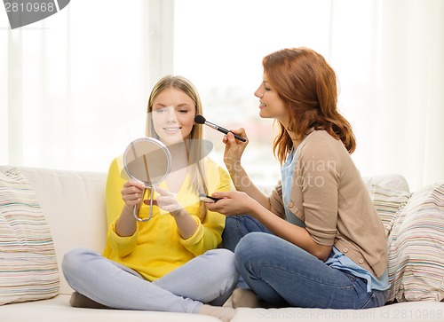 Image of two smiling teenage girls applying make up at home