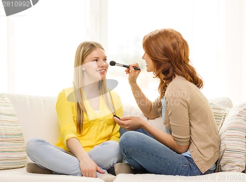 Image of two smiling teenage girls applying make up at home