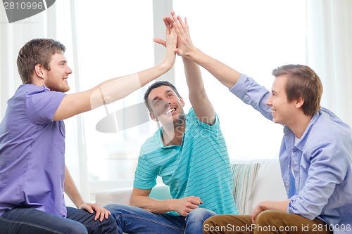 Image of smiling male friends giving high five at home