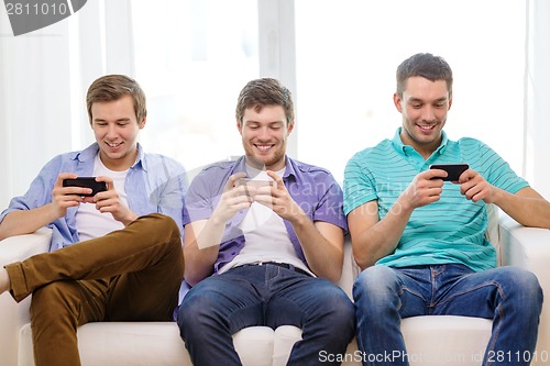 Image of smiling friends with smartphones at home