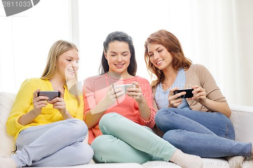 Image of smiling teenage girls with smartphones at home