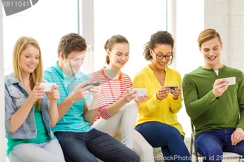 Image of smiling students with smartphone texting at school