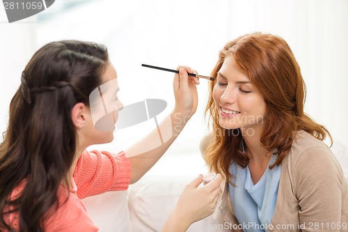 Image of two smiling teenage girls applying make up at home