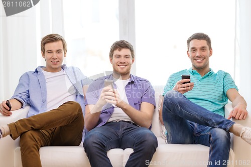 Image of smiling friends with smartphones at home