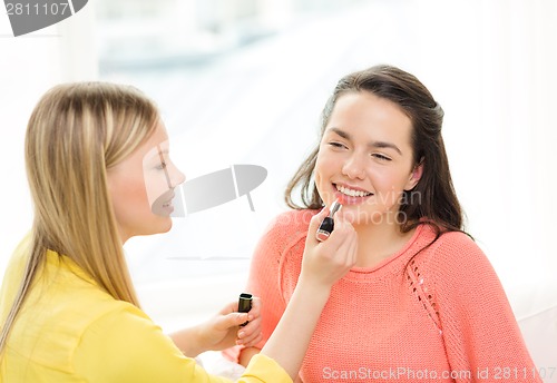 Image of two smiling teenage girls applying make up at home