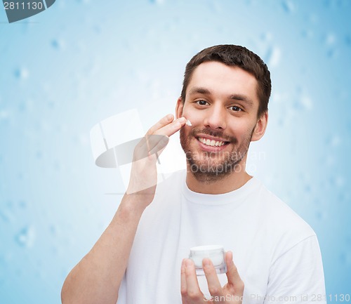 Image of beautiful smiling man applyin cream