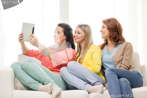 Image of three smiling teenage girls with tablet pc at home
