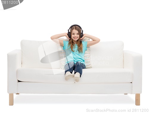 Image of smiling little girl in headphones sitting on sofa