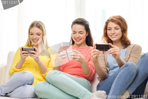 Image of smiling teenage girls with smartphones at home