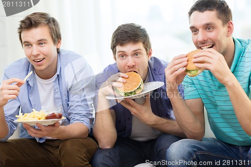 Image of smiling friends with soda and hamburgers at home