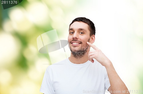 Image of smiling young handsome man pointing to cheek